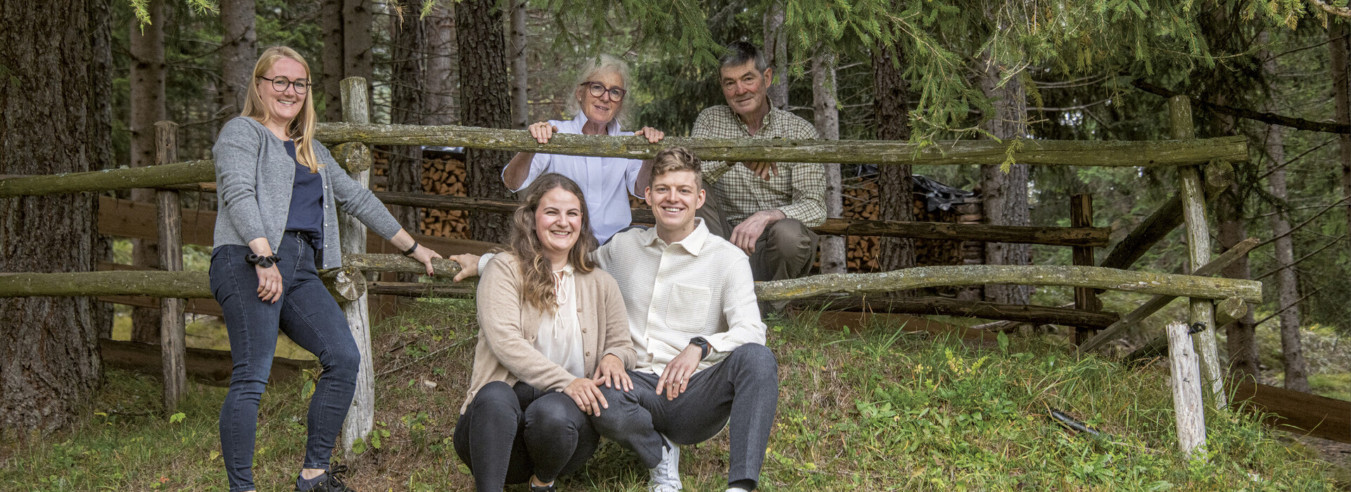 Familie von fünf Personen vor einem Holzzaun im Wald auf einer Wiese.