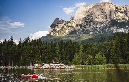 Mountain lake with pedal boaters, forested shore, and prominent rocky massif in the background.