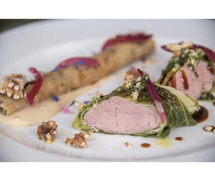 Sliced meat wrapped in savoy cabbage with walnuts and sauce arranged on a white plate.