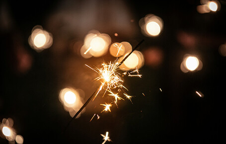Funkelnde Wunderkerze vor unscharfem Hintergrund mit Lichtpunkten.